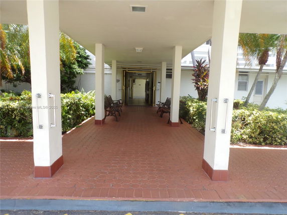 Outdoor covered entrance area with benches and plants.