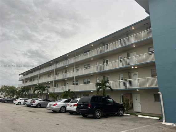 Front view of a multi-story building with balconies and parking in front.