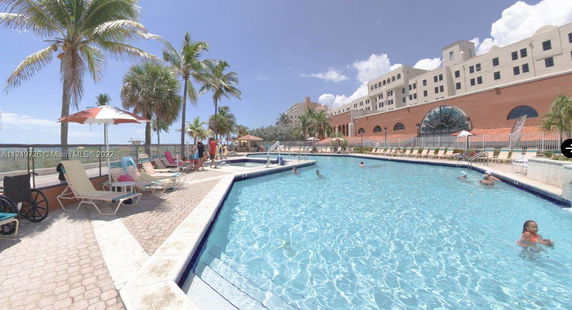 Outdoor swimming pool area with surrounding lounge chairs and palm trees.