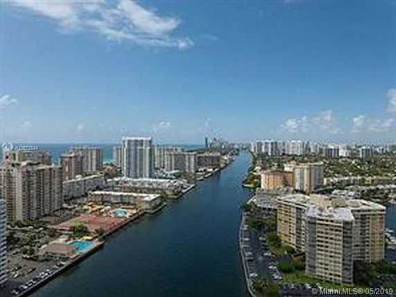 Panoramic view of a canal surrounded by high-rise buildings, with the ocean in the distance.