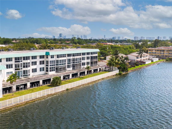 View of a multi-story waterfront building with a fenced yard by a large body of water.