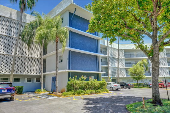 Front view of a multi-story residential building with blue accents and surrounding parking area.