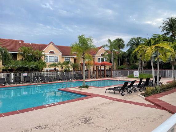 Outdoor swimming pool area with lounge chairs and a view of adjacent buildings with red roofs.