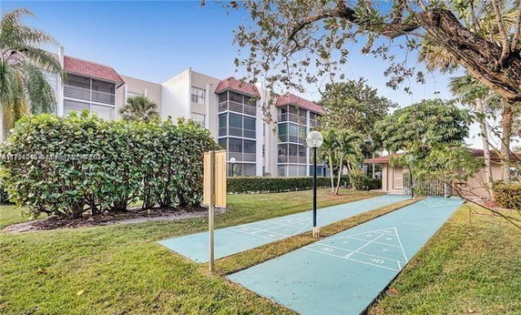 Exterior view of a multi-story residential building with screened balconies and a shuffleboard court in the foreground.