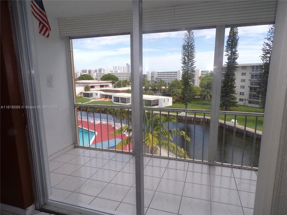 View from a balcony showing a swimming pool, trees, and nearby buildings.