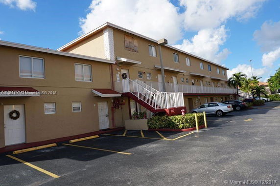 Front view of a multi-story apartment building with external stairs and parking area.