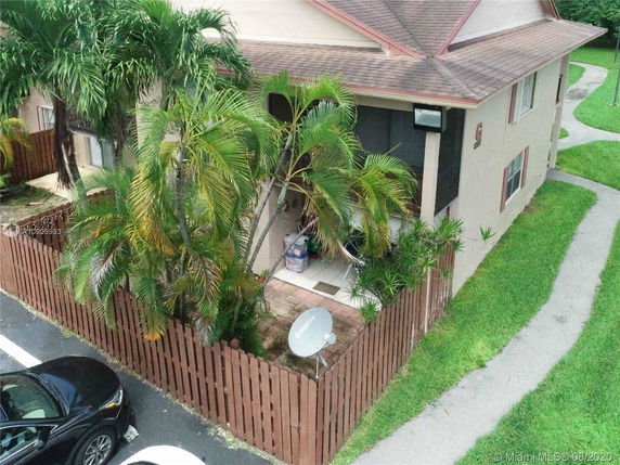 Partial view of a two-story house with a fenced patio and palm trees.