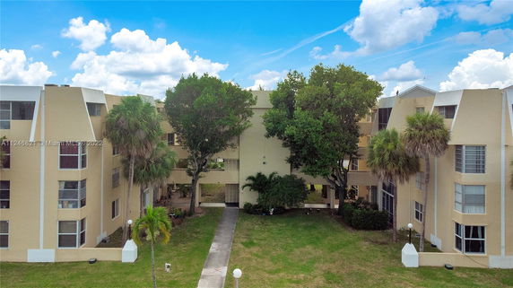 Front view of a multi-story residential building with trees and grass in front.