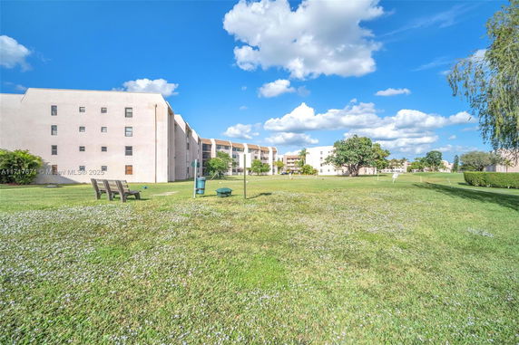 Exterior view of a multi-story building with a grassy area and scattered benches.