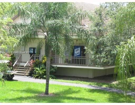 Front view of a single-story house with a porch and stairs, surrounded by trees and plants.