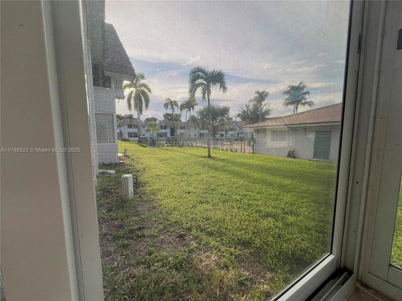 View from inside looking out towards a grassy outdoor area with buildings and palm trees.