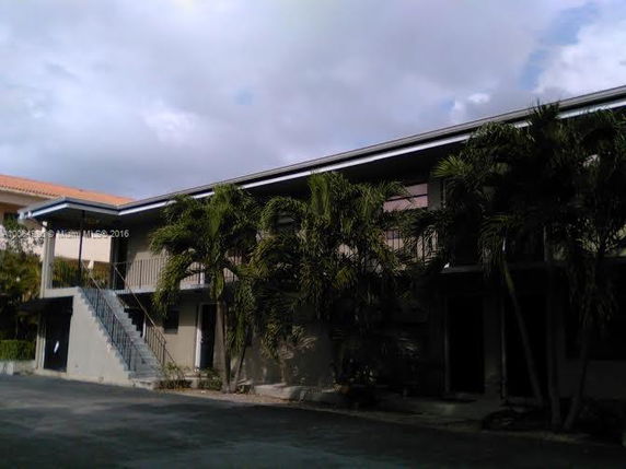 Front view of a two-story building with external stairs and surrounding palm trees.