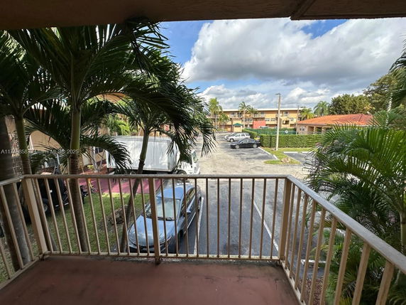 View from a balcony looking out towards a parking area with cars and palm trees, surrounded by residential buildings.