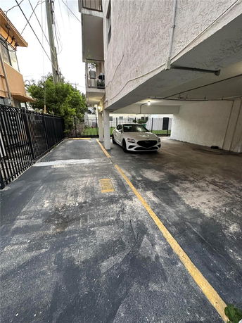 Covered parking area beneath a building with a white car parked.