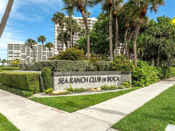 Front view of a multi-story residential building with palm trees and a sign reading 'Sea Ranch Club of Boca'.