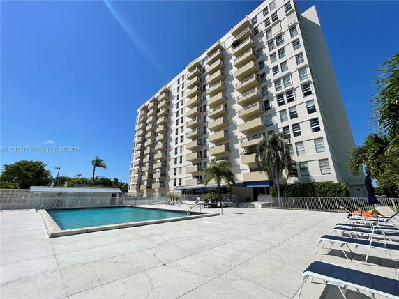 Outdoor swimming pool area in front of a multi-story residential building.
