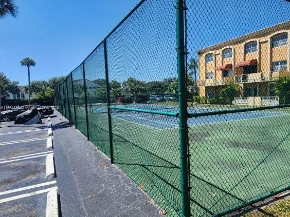 Image of a tennis court surrounded by a fence next to a parking area.