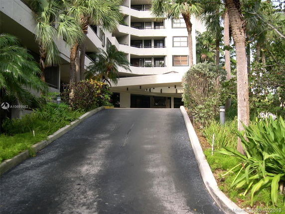 Front view of a multi-story building with a driveway lined with palm trees and greenery.