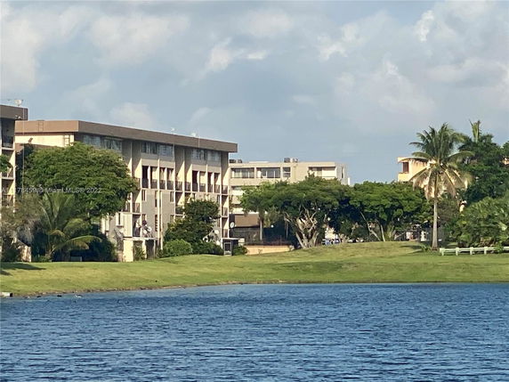 View of a multi-story building near a body of water, surrounded by trees.