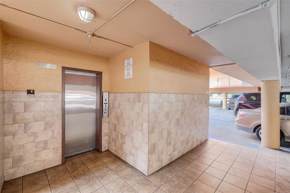 Elevator area adjacent to a covered parking space with tiled flooring and walls.