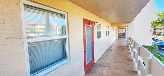 View of a building corridor with doors and windows facing a parking area.