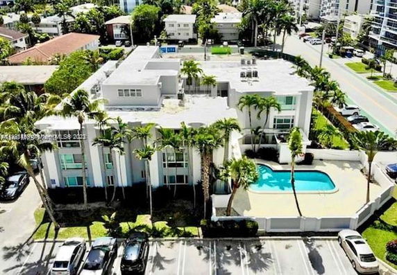 Aerial view of a multi-story building with a swimming pool and parking area.