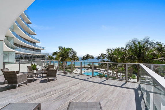 Outdoor panoramic view from a balcony overlooking a pool and ocean.