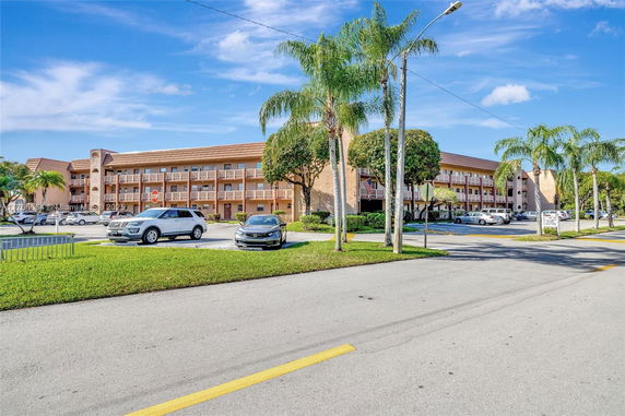 Front view of a multi-story building with balconies, surrounded by a parking lot and palm trees.