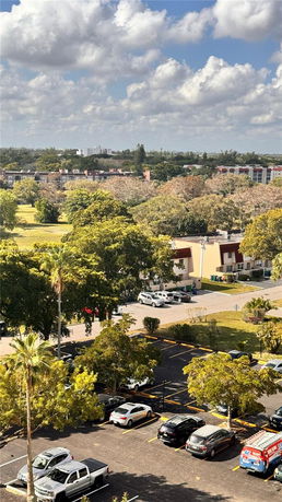 Aerial view of a parking area surrounded by trees and distant buildings.