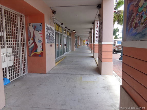 Covered walkway alongside a row of shops with murals on the walls.