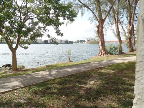 View of a lake with buildings in the distance, framed by trees and a walking path.