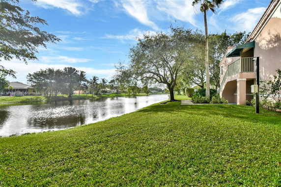 View of a grassy area by a water body with trees and a partial view of a building.