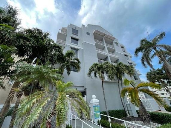 Front view of a multi-story residential building with balconies and palm trees.