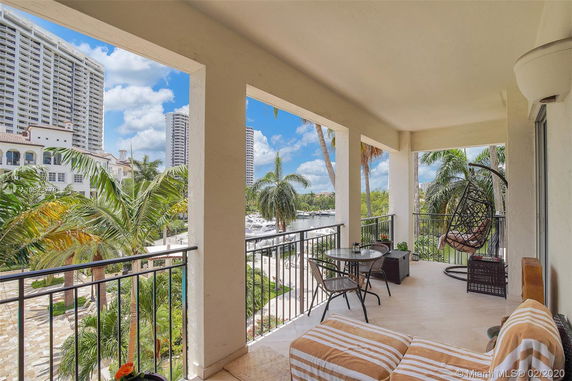Covered balcony with outdoor furniture overlooking nearby buildings and palm trees.