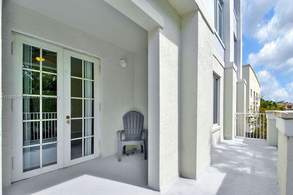Exterior view of a building with a balcony, featuring a chair and glass doors.