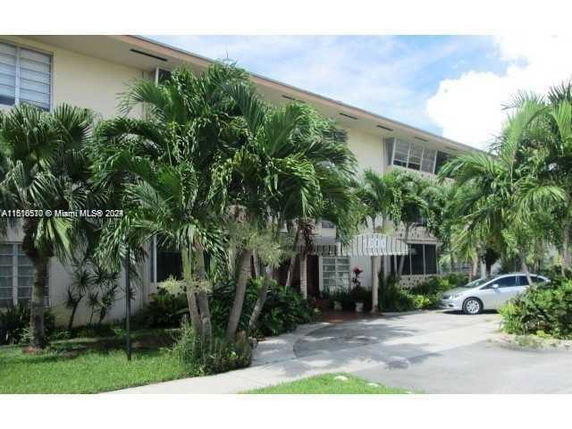 Front view of a two-story building with a canopy entrance and surrounding tropical landscaping.