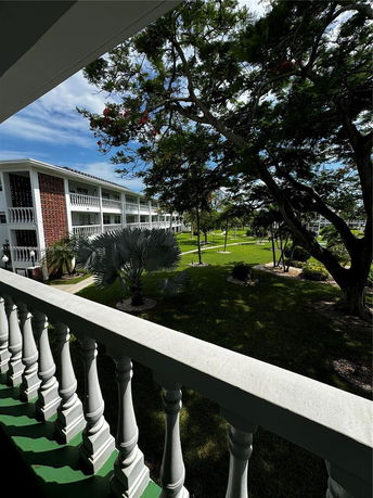 View from a balcony overlooking green lawns and trees with a multi-story building in the background.