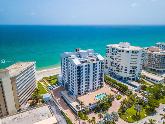 Aerial view of a tall beachfront condominium with surrounding buildings and ocean in the background.