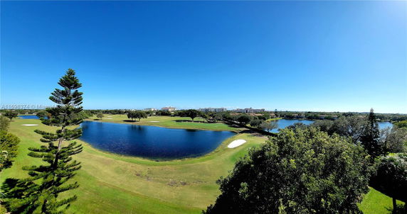 Panoramic view of a landscape with a lake, golf course, and distant buildings.