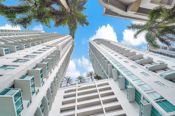 Upward view of two tall residential buildings with balconies and palm trees.