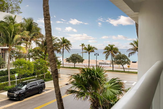 View from a building overlooking a road, palm trees, and the ocean.