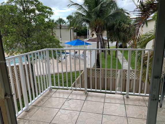 View from a balcony looking out towards a swimming pool, surrounded by palm trees and a pathway.