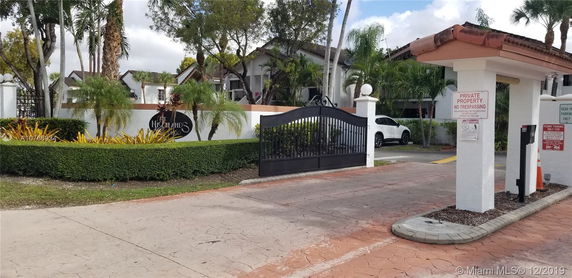 Front view of a residential complex entrance with a gate and signage.