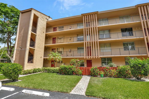 Front view of a four-story apartment building with balconies and a small garden.