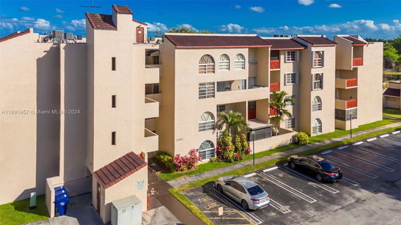 Front view of a multi-story residential building with arched windows and a parking area.