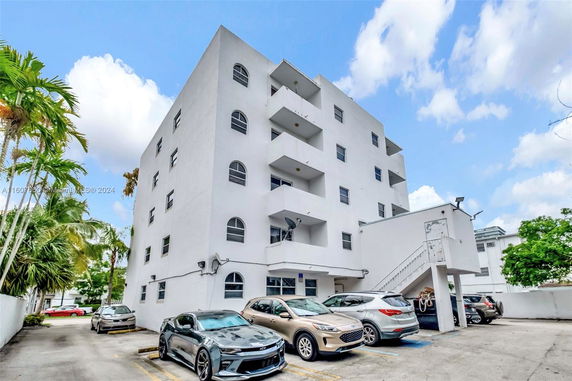 Front view of a multi-story residential building with multiple balconies and parked cars.