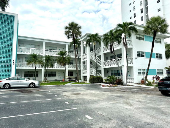 Front view of a two-story building with decorative railings and palm trees in the front.