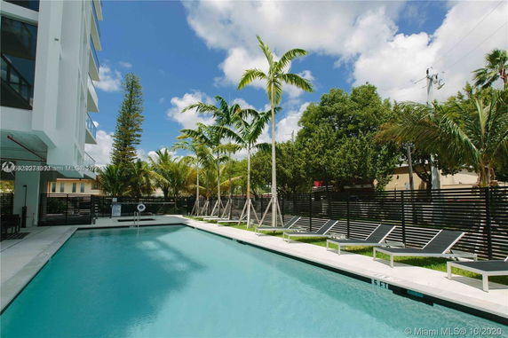 Outdoor swimming pool area with sun loungers and palm trees next to a building.