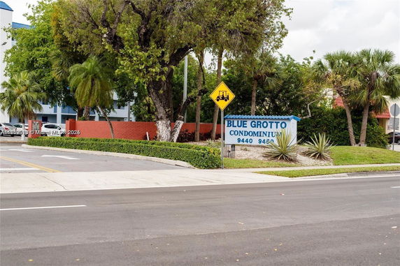 View of the entrance sign for Blue Grotto Condominium with surrounding trees and greenery.