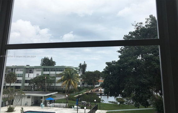 View from a window overlooking a residential complex with green areas and a water body.